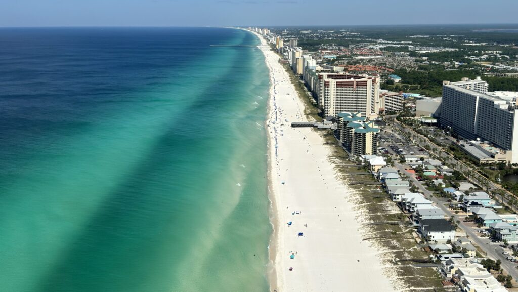 Luftaufnahme von Panama City Beach, Florida. Zu sehen ist die smaragdgrüne Küste mit ihrem weißen Sandstrand, den türkisblauen Wellen und den zahlreichen Hochhäusern entlang der Küste.