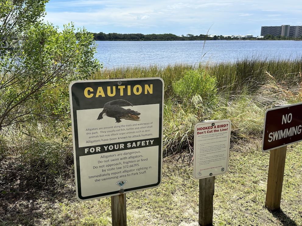 Warnschilder in einem Naturpark in Panama City Beach, Florida, mit Hinweisen auf Alligatoren und Verhaltensregeln in der Umgebung eines Sees.