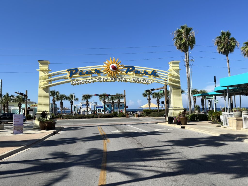 Eingangsbogen des Pier Parks in Panama City Beach, Florida, mit Palmen und einem klaren blauen Himmel im Hintergrund.