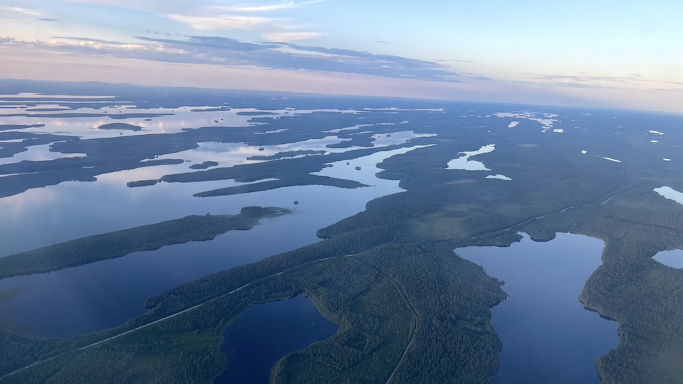 "Luftaufnahme von Finnlands weitläufigen Seen und Wäldern während eines Flugs von Helsinki nach Kuusamo bei Sonnenuntergang."