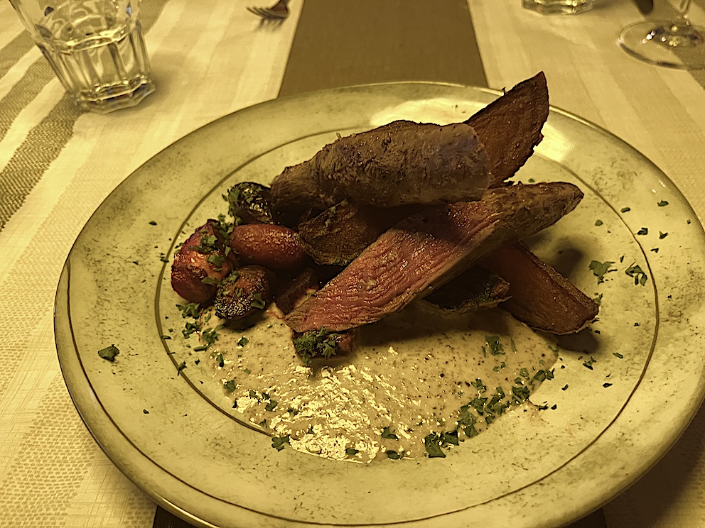 Rentierfleisch auf einem Teller, begleitet von Kartoffeln und Gemüse, angerichtet mit einer cremigen Soße.