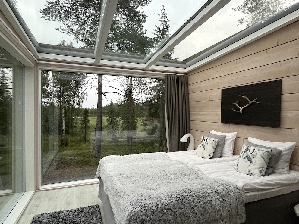 Schlafzimmer mit Glasdecke und großen Fenstern in einem modernen Glas-Iglu, umgeben von Wald im Iisakki Glass Village.
