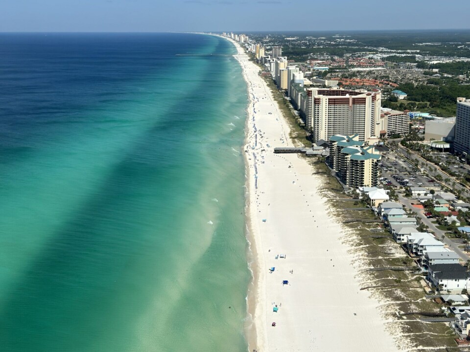 Luftaufnahme von Panama City Beach, Florida. Zu sehen ist die smaragdgrüne Küste mit ihrem weißen Sandstrand, den türkisblauen Wellen und den zahlreichen Hochhäusern entlang der Küste.