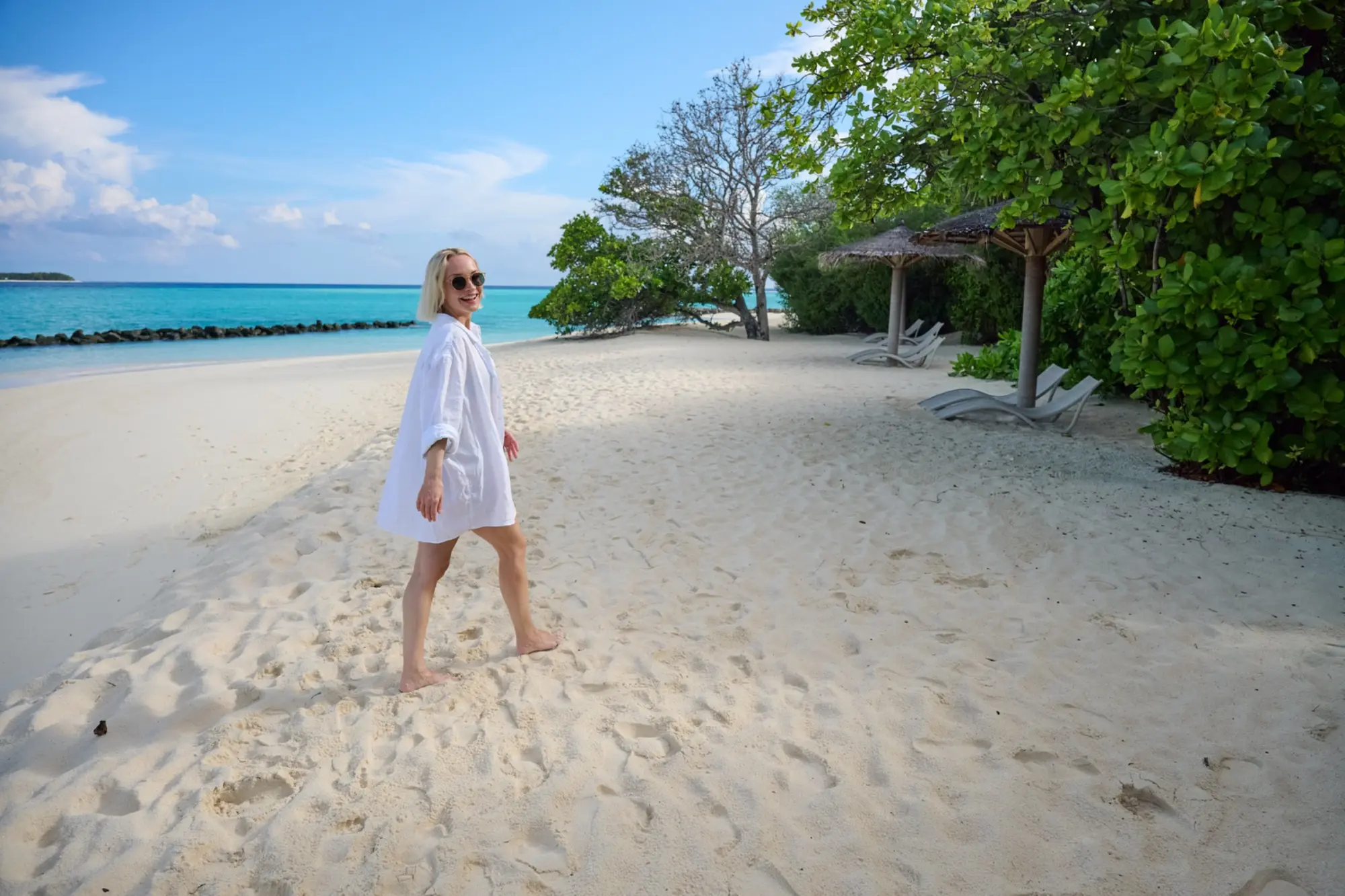 Janin Ullmann spaziert barfuß in einem weißen Strandlook über die Insel.
