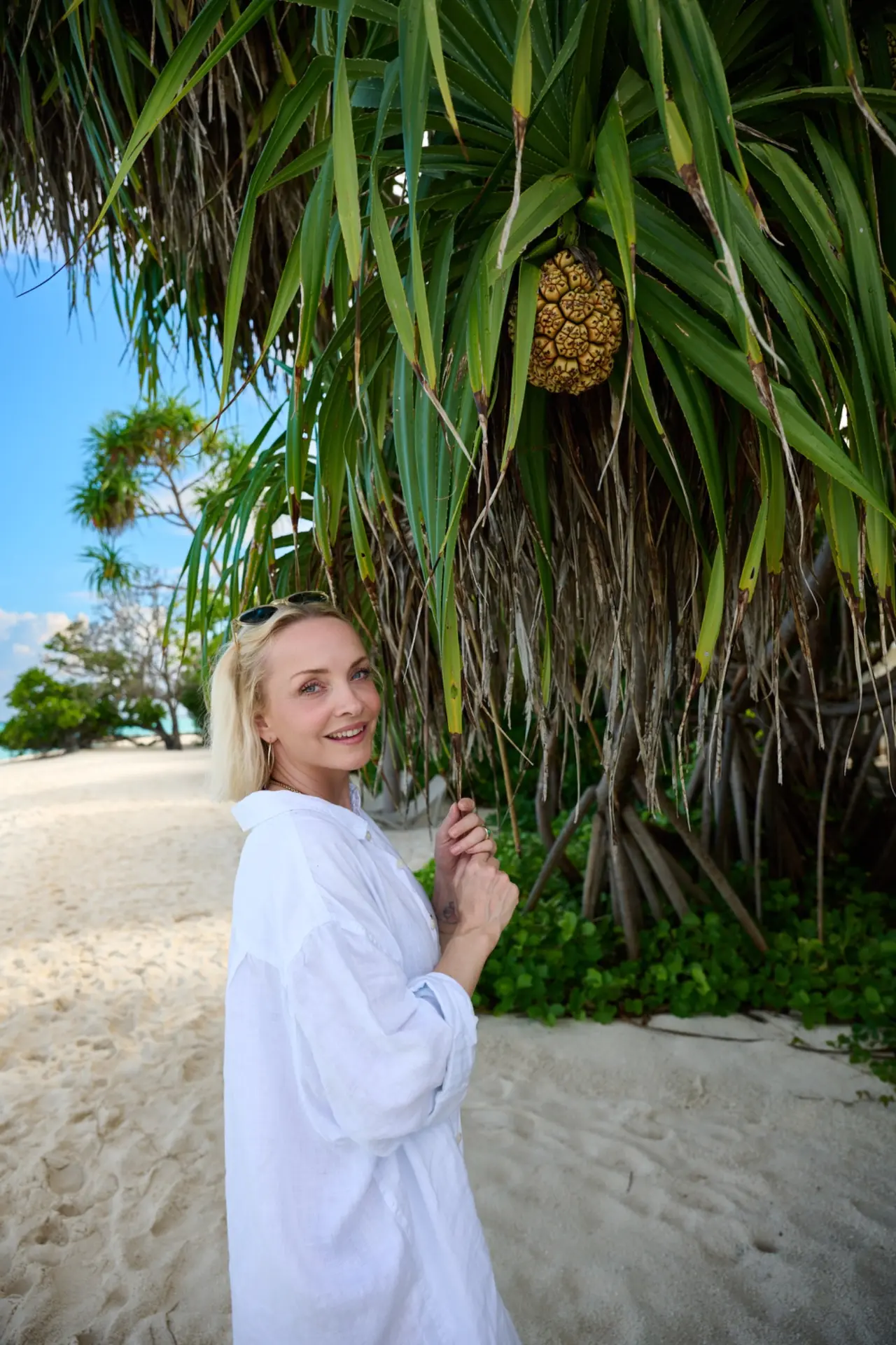 Janin Ullmann steht in einem weißen Strandlook unter einer Palme.