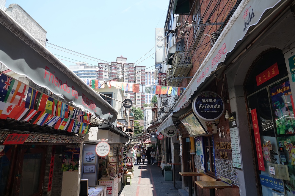 Eine enge Gasse im Tianzifang-Viertel von Shanghai, mit Bars, internationalen Fahnen und kleinen Geschäften.
