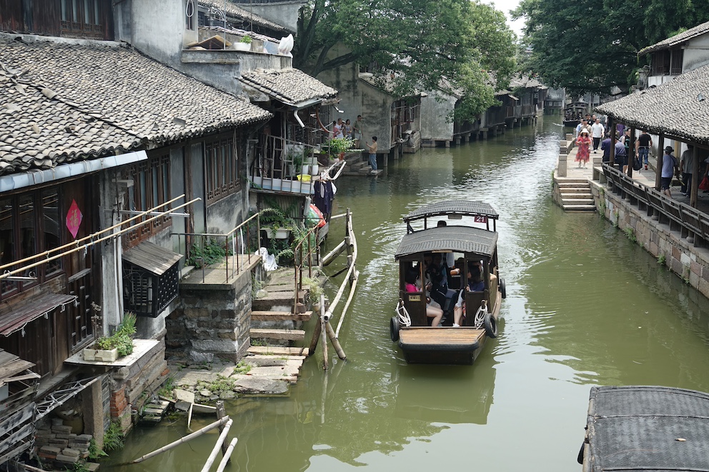 Ein traditionelles chinesisches Ruderboot fährt durch die Wasserstraßen der historischen Stadt Wuzhen, gesäumt von alten Häusern
