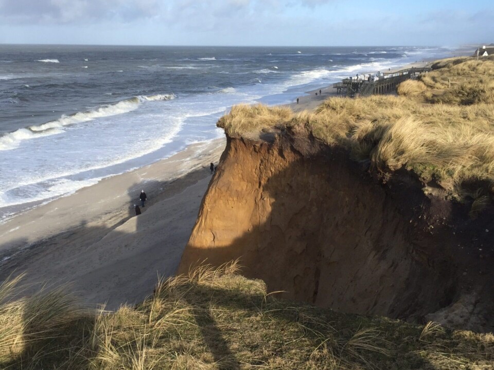 Steilküste auf Sylt mit Blick auf die Nordsee, sandige Dünen und Gräser, herbstlicher Himmel und hohe Wellen bei windigem Wetter.