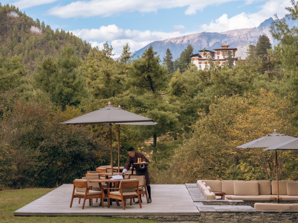 Terrasse der Amankora Paro Lodge mit Blick über Kiefern und Berge zur Festung Drukgyel Dzong.