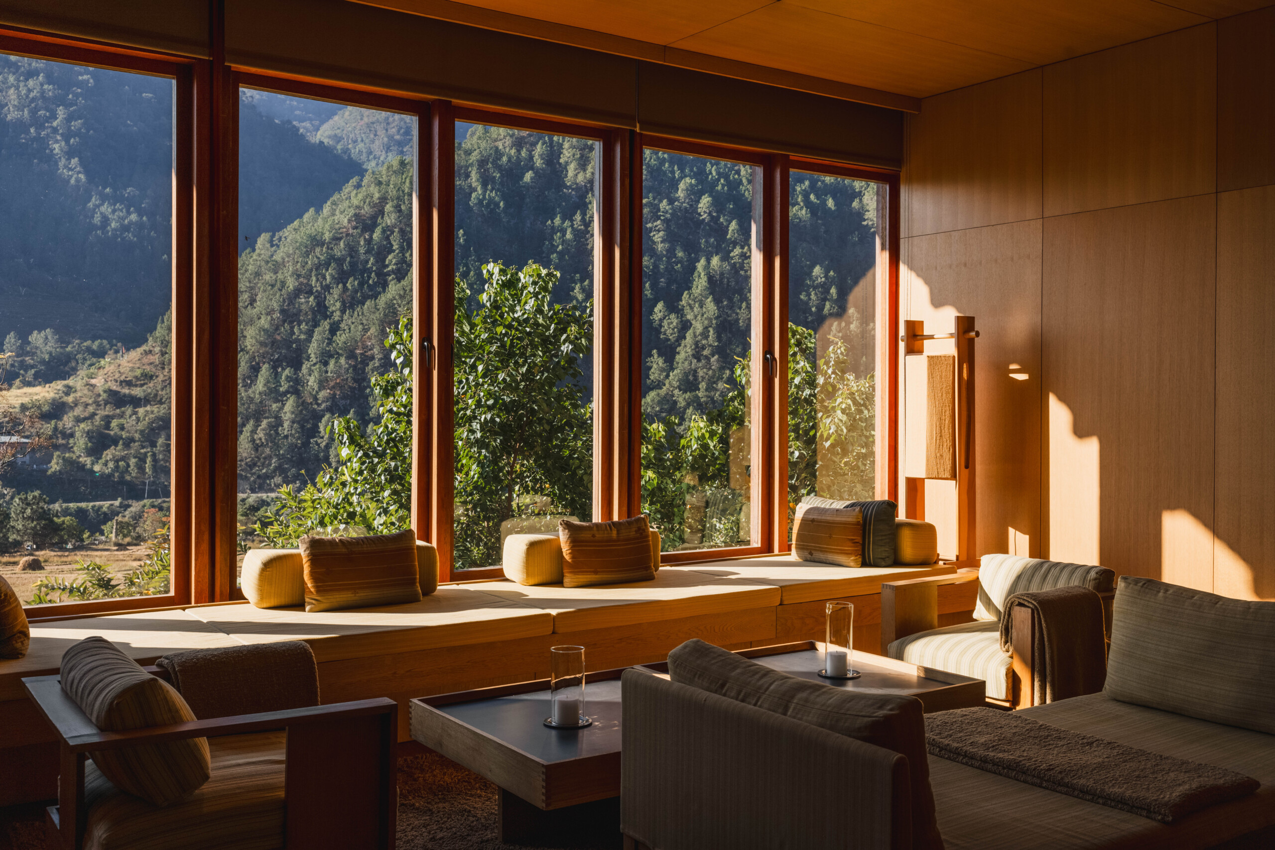Wohnbereich der Mo Chhu Suite in Amankora Punakha mit Holzverkleidung und großen Fenstern zum bewaldeten Tal.