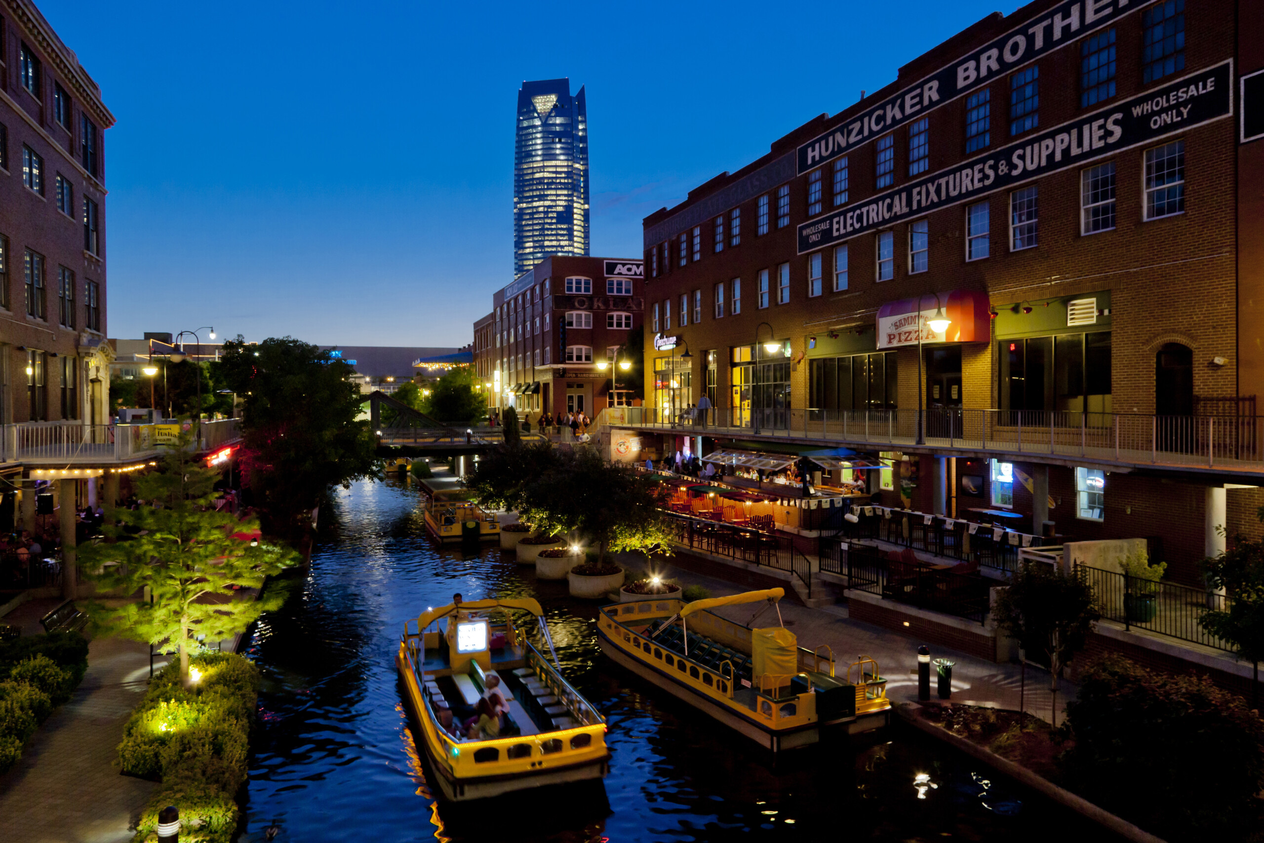 Beleuchtete Backsteinfassaden und ein Wassertaxi am Bricktown Canal in Oklahoma City