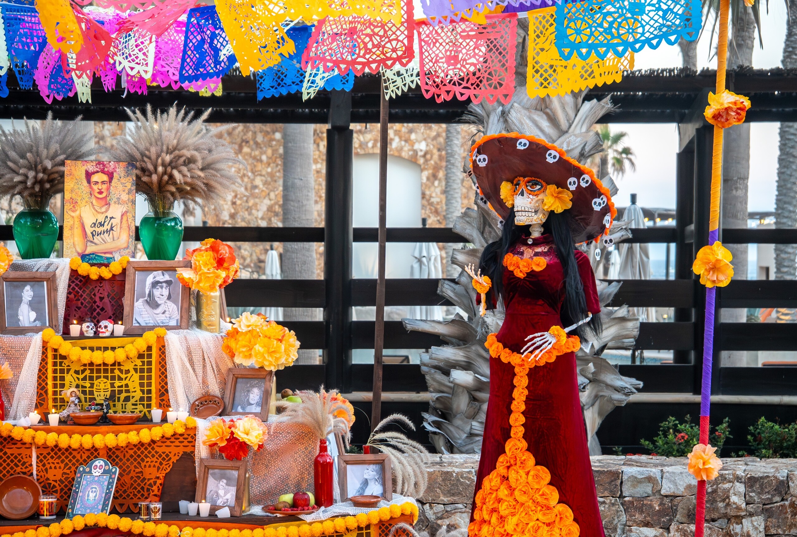 Ofrenda mit Familienfotos, Blumen und Papierdekoration neben einer Catrina-Figur im roten Kleid.