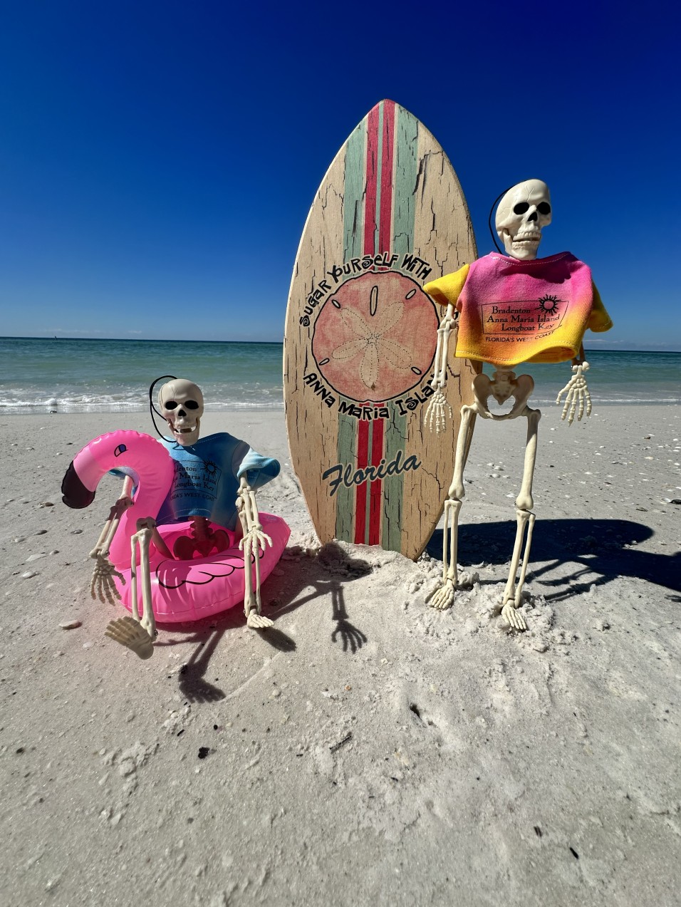 Zwei dekorative Skelette mit Surfbrett am weißen Sandstrand