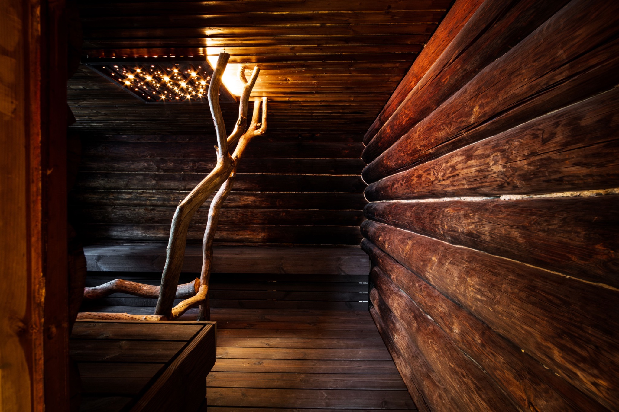 Dunkle Blockbohlen, Holzbänke und ein beleuchteter Baumstamm in der Kelo-Sauna von Lykynlampi.