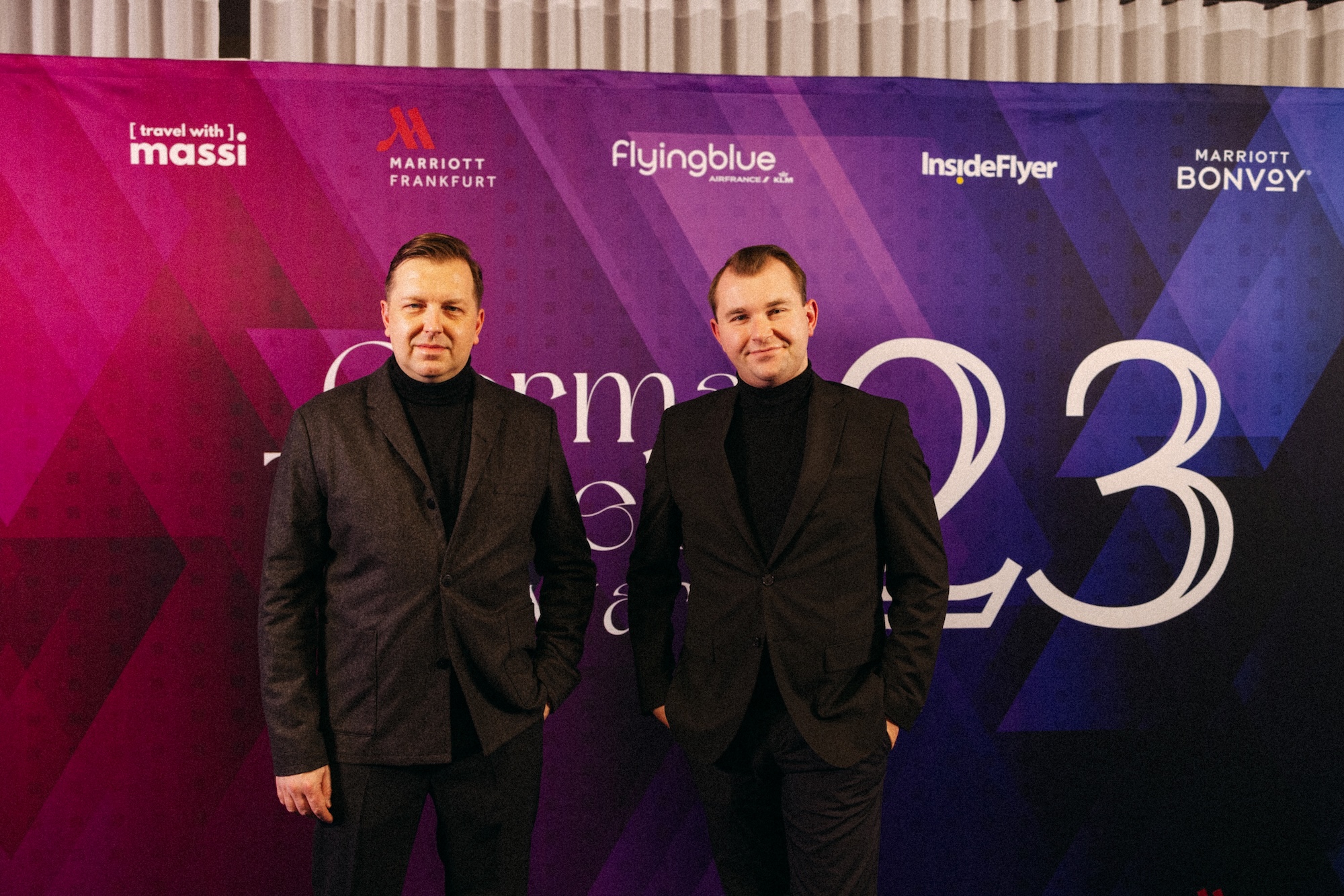Marcel Wladasch und Steffen Hager vor einer Veranstaltungswand der German Traveller Awards 2023.