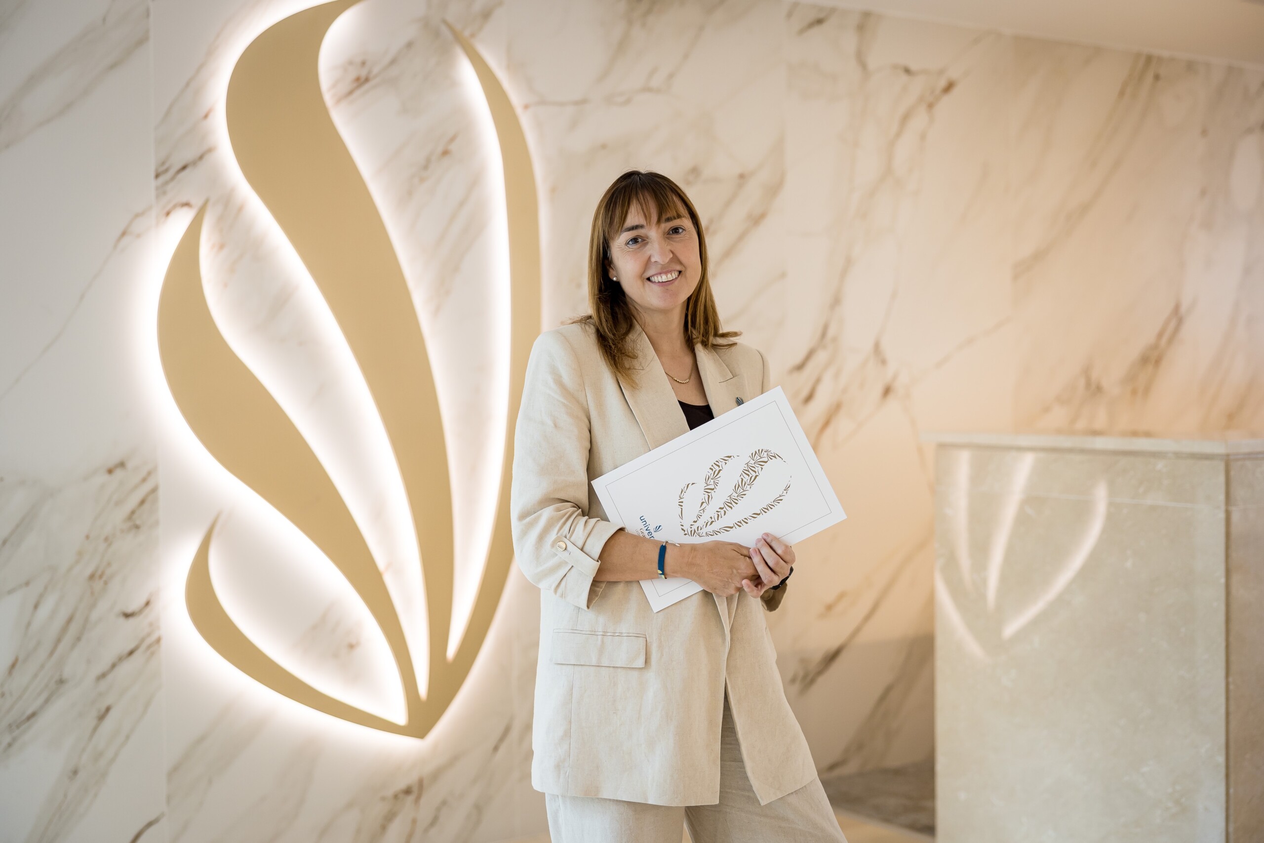 Maria Elena Oliver Lladó steht mit einer Mappe vor einer beleuchteten Wand im Universal Grand Leon & SPA.
