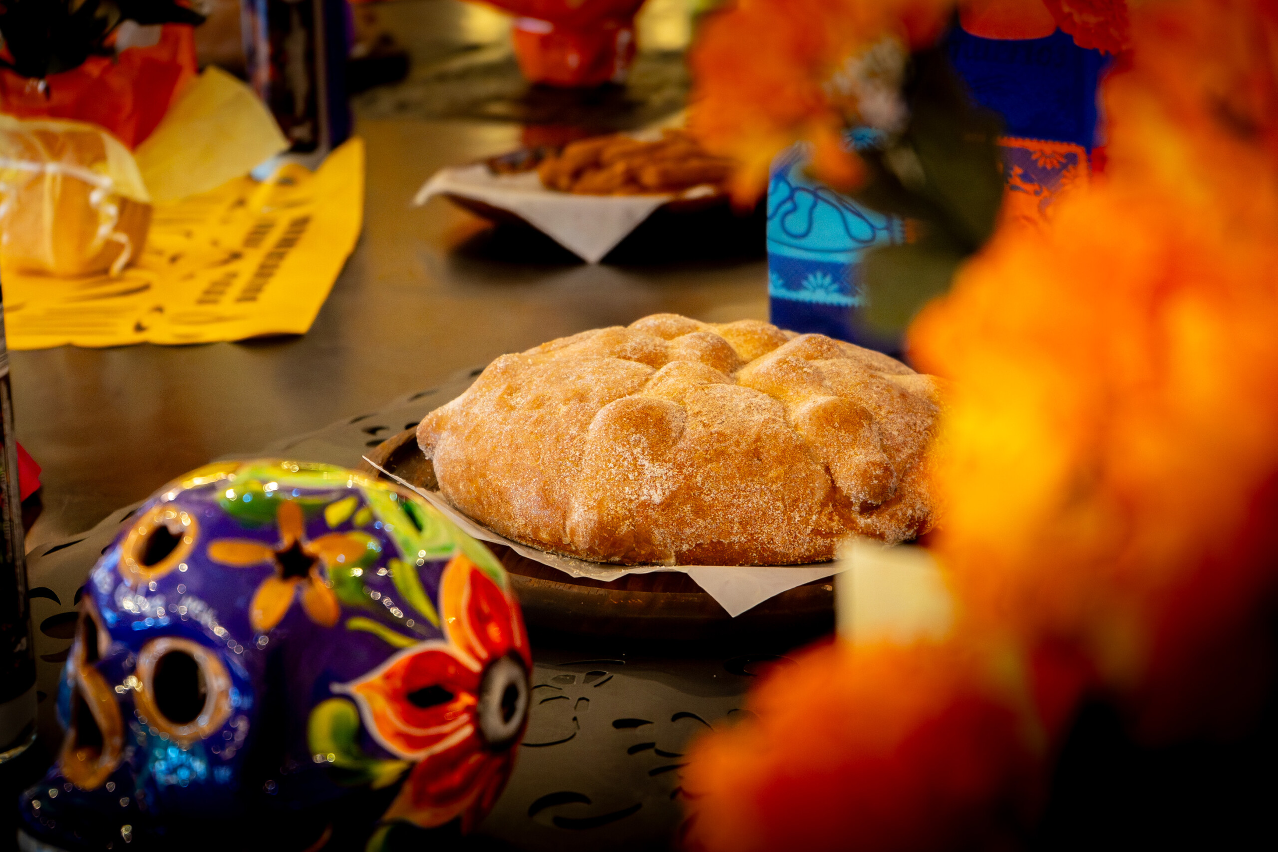 Pan de Muerto neben einem bunten Totenkopf und orangefarbenen Blüten.
