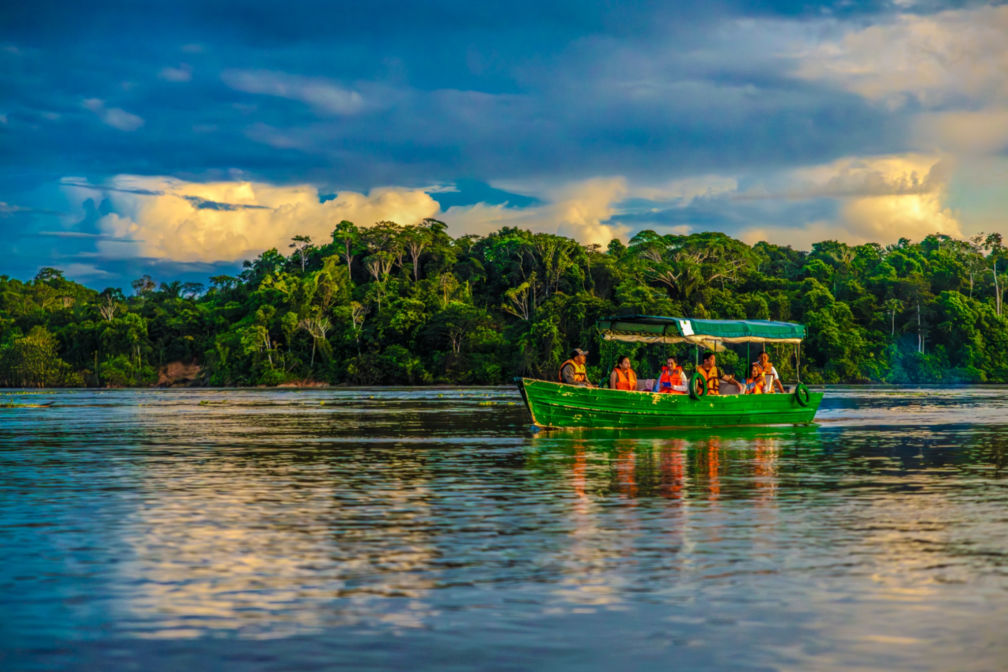 Ein überdachtes Boot mit Passagieren fährt vor dichtem Regenwald über einen Fluss in Peru.